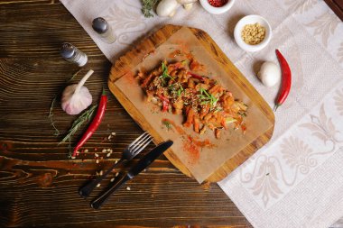 Acı soslu ve baharatlı deniz ürünleri mürekkep balığı. Koyu bir masanın üstünde, çatal bıçak takımı, bir baş sarımsak, beyaz şampiyon, bir çift biber ve tuz, bir biberiye dalı..