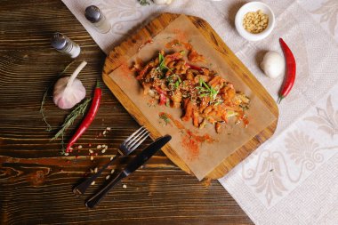 Acı soslu ve baharatlı deniz ürünleri mürekkep balığı. Koyu bir masanın üstünde, çatal bıçak takımı, bir baş sarımsak, beyaz şampiyon, bir çift biber ve tuz, bir biberiye dalı..