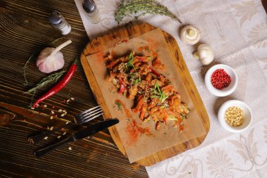 Acı soslu ve baharatlı deniz ürünleri mürekkep balığı. Koyu bir masanın üstünde, çatal bıçak takımı, bir baş sarımsak, beyaz şampiyon, bir çift biber ve tuz, bir biberiye dalı..