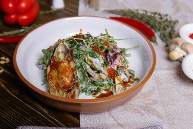 Midyeli salata, roka, kırmızı havyar, yuvarlak tabakta karides çatal bıçak takımı, biber-tuz buharı, bütün kırmızı biber, acı biber, süs olarak baharat. Koyu ahşap bir masanın üzerindeki keten peçete..