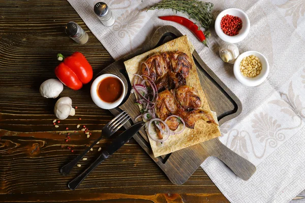 Koyu bir tezgahın üzerinde, açık keten bir peçete, bir kesme tahtası üzerinde dört bıldırcın kızarttı kırmızı soğan halkalarıyla birlikte pita ekmeğinde, keten peçetede, kırmızı biber, biberiye dalında.