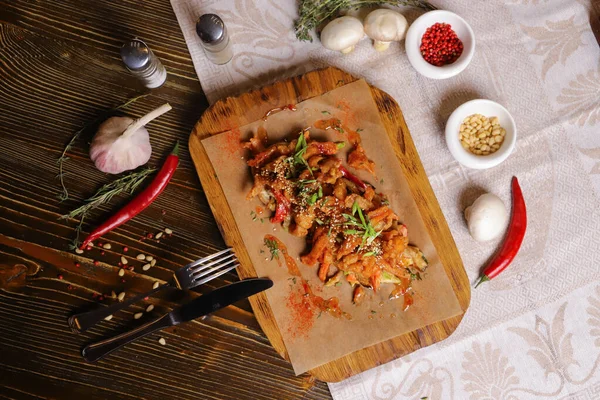 Acı soslu ve baharatlı deniz ürünleri mürekkep balığı. Koyu bir masanın üstünde, çatal bıçak takımı, bir baş sarımsak, beyaz şampiyon, bir çift biber ve tuz, bir biberiye dalı..