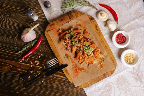 Acı soslu ve baharatlı deniz ürünleri mürekkep balığı. Koyu bir masanın üstünde, çatal bıçak takımı, bir baş sarımsak, beyaz şampiyon, bir çift biber ve tuz, bir biberiye dalı..