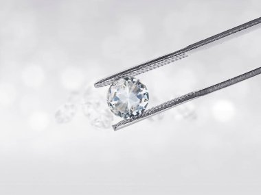 Elmas cımbızla tutulan göz kamaştırıcı elmas beyaz arka planda, yerde yansımalar var. Bir sürü boşluk