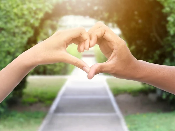 couple making heart shape with hands in park