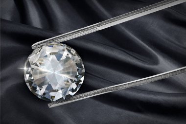 Shiny diamond on black fabric background held in diamond tweezers