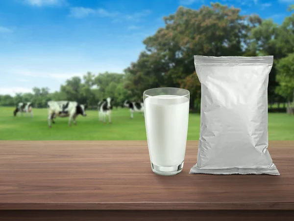 ガラスの新鮮な牛乳 暗い木製のテーブルの上に箔食品包装 牧草地に牛と背景がぼやけている 健康的な食事 — ストック写真