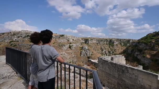 意大利Basilicata的Matera 2021年8月 两个男孩欣赏马德拉洞穴的风景并对其进行评论的镜头 从男孩到景观的泛运动 — 图库视频影像