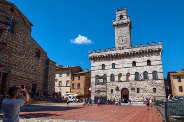 Montepulciano, Toskana, İtalya. Ağustos 2021. Piazza grande tarihi merkezin ana meydanı, kulesi olan ve saati kanıt olan belediye binası. Bir turist akıllı telefonuyla fotoğraf çeker.