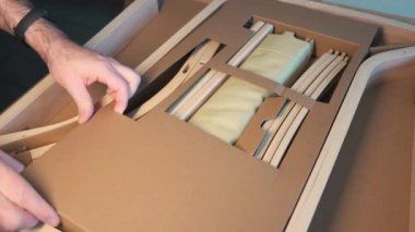 Bir sandalyenin ambalajı üzerindeki yakın çekim görüntüleri. Eller monte edilecek parçalara ulaşmak için kartondan ayırır..