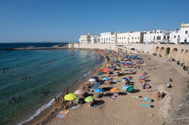 Gelibolu, Puglia, İtalya. Ağustos 2021. Eski kasabadaki kumlu sahil, yıkanan ve güneşlenen insanlarla dolu..