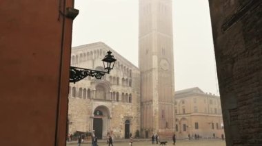 Parma, Emilia-Romagna, Italy. January 2022. Amazing pov footage walking towards the fog-shrouded Duomo square. The cathedral and the baptistery dominate the scene, people cross the square.