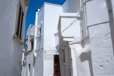 Ostuni, Puglia, İtalya. Ağustos 2021. Eski şehrin beyaz sokaklarından birinin muhteşem manzarası var. Mekanın eşsiz cazibesi baskın renk kadar beyaz huzur ve sükunet hissi..