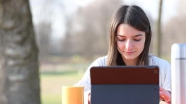 Parkta uzaktan çalışan, yeşil bardaktan içen ve dizüstü bilgisayarında yazan güzel bir kadının portresi. Rüzgar saçlarını hafifçe hareket ettiriyor. Arka planda bulanık insanlar.