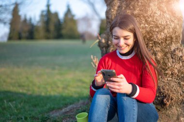 Çekici bir genç esmer kadın parktaki bir ağacın dibinde oturuyor. Bir mesaj alıyor tasasız, iletişim teknolojisi kavramı.