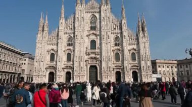 Milan, İtalya, Mart 2022. Katedral meydanının eğik görüntüleri. Güneşli bir günde açık renkli cephe sahneye hakim olur. Bazıları yürür ve diğerleri eğlenmek için durur..