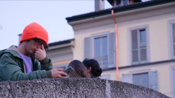 Mladý Běloch Brýlemi Oranžovou Čepicí Používá Svůj Mobilní Telefon Zatímco — Stock video