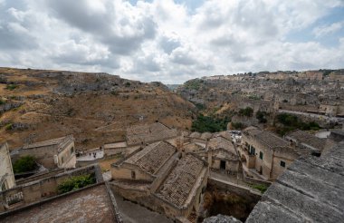 Matera, Basilicata, İtalya. Ağustos 2021. Matera taşlarının panoramik manzarası muhteşemdi. Soldaki tepede antik mağaralar tanınabilir durumda. Sağda eski karanlık taş evler..