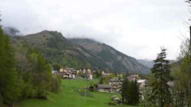 Beaulard, Piedmont, İtalya. Mayıs 2022. Dağ kasabasının inanılmaz eğik görüntüleri. Alçak yay bulutları vadiyi çevreleyen dağların tepesini kaplar. Dağ yolculuğu resmi.