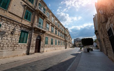 Trani, Puglia, İtalya. Ağustos 2021. Tarihi merkezde yeşil pencereli periyot evleri tarafından gözden kaçırılan büyüleyici bir cadde. Mavi gökyüzü ve beyaz bulutlarla güzel bir yaz günü.