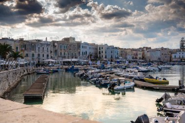 Trani, Puglia, İtalya. Ağustos 2021. Marinanın güzel manzarası renkli cepheli evlerle çevrili, bulutların arasından süzülen ışıklarla dolu dramatik bir gökyüzü..
