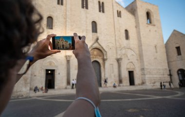 Bari, Puglia, İtalya. Ağustos 2021. Aziz Niklas Kilisesi 'nin heybetli cephesi, Roma Katolik tarzında. Meydandaki insanlar. Genç bir adam cep telefonuyla fotoğraf çekiyor.