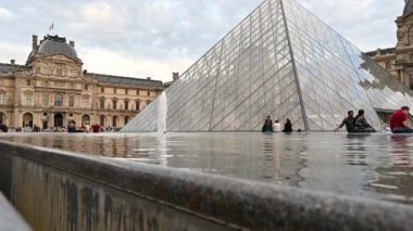 Fransa, Paris, Haziran 2022. Güzel bir günde Louvre 'un büyük meydanı, büyük cam piramit fıskiyenin suyuna yansıyor, turistler.