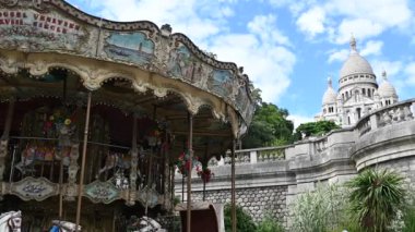 Paris, France, June 2022. Pan footage with nice view of the Sacre Coeur basilica and the vintage carousel at the base of the Montmartre hill. Beautiful summer day with blue sky and white clouds.