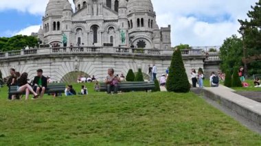 Paris, France, June 2022. Tilt footage from the Montmartre hill lawn to the Sacre Coeur basilica. People relax on the lawn enjoying the beautiful summer day.