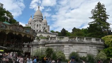 Paris,France,June 2022.Footage with a nice view of the Sacre Coeur basilica, pov of the tourist who walks the open space at the base of the Montmartre hill and looks up towards it,visible the carousel