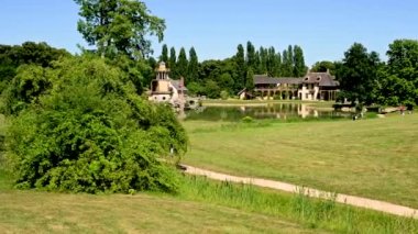 Versailles, Paris, Fransa, Haziran 2022. Petit Trianon parkındaki Hameau de la Reine 'in kamera görüntüleri çok güzel. İnsanlar çayırların ortasında patikalardan yürür. Güzel bir yaz günü.