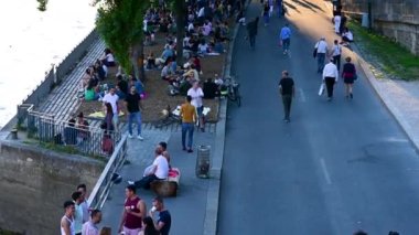 Paris, France, June 2022. Tilt footage on the bank of the seine in the old town at the golden hour. People stroll along the bank, groups of people stop sitting on the benches or under the trees.