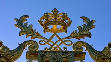 Versailles,Paris,France,June 2022.Detail of the gate of the palace: the golden crown expresses all the beauty and splendor of the palace, a symbol of the king's power. Some birds fly in the background