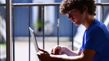 Portrait of a young caucasian man sitting at the attic window, he is working on the laptop. Blurred background. Concept of using technology, remote study and work, work and study at home.