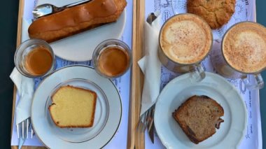 Paris, France. A rich breakfast with typical sweets and cappuccino and coffee. The hand grabs a biscuit and then the cup of coffee. View from above.