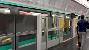 Paris, France, June 2022. A train passes by at a metro station. A traveler walks off along the quay.