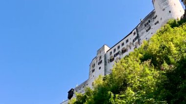 Salzburg, Avusturya, Ağustos 2022. Hohensalzburg kalesinin geniş açı mercekli ve tava hareketli görüntüleri güzel. Aşağıdan bakış açısı onun ihtişamını arttırır. Güzel bir yaz günü.