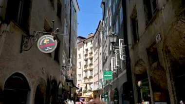 Salzburg, Avusturya, Ağustos 2022. Eski kasabanın alışveriş caddesinde yürüyen güzel bir POV filmi. İnsanlar arasında yürürken üstümüzdeki metal işaretleri....