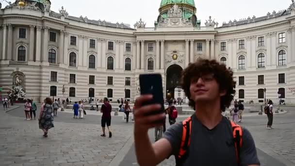 ウィーン オーストリア 2022年8月 ミカエルプラッツ広場のスローモーション映像 若い男はその印象的な建物でシーンを支配する彼の後ろに宮殿と自撮りを取ります — ストック動画