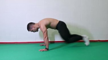 Genç kaslı erkek sporcu, dağ tırmanışı yaparken üstsüz antrenman yapıyor. Beyaz duvarlı arkaplan, boşluğu kopyala.