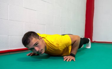 Şınav çeken ve kameraya bakan kararlı genç bir adam. O, sarı bir gömlek ve siyah bir tulum giydi. Boşluğu kopyala