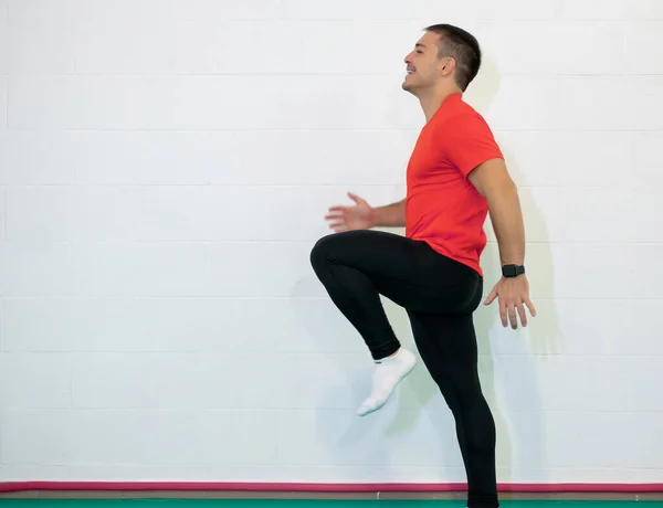 Work out. Young caucasian male athlete sprinter running, exercising indoors, jogging in training room, side view. Red shirt and black jumpsuit.  Copy space