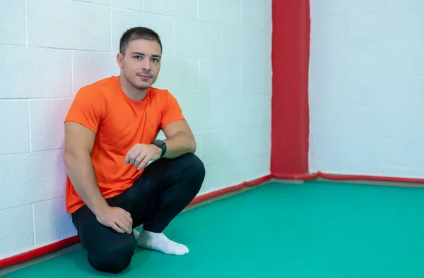 Young caucasian man crouching pose looking into the camera in a moment of break from fitness exercises in the gym. Concept of health, fitness, positivity and success.