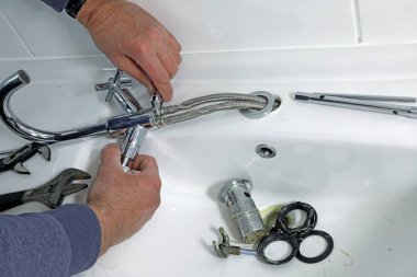 Bir tesisatçı eski musluğu ve atığı bir lavabodan temizliyor..