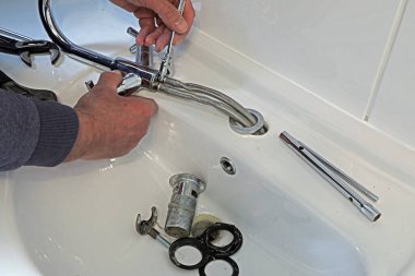 Bir tesisatçı eski musluğu ve atığı bir lavabodan temizliyor..