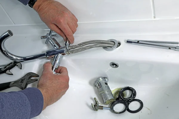 Bir tesisatçı eski musluğu ve atığı bir lavabodan temizliyor..