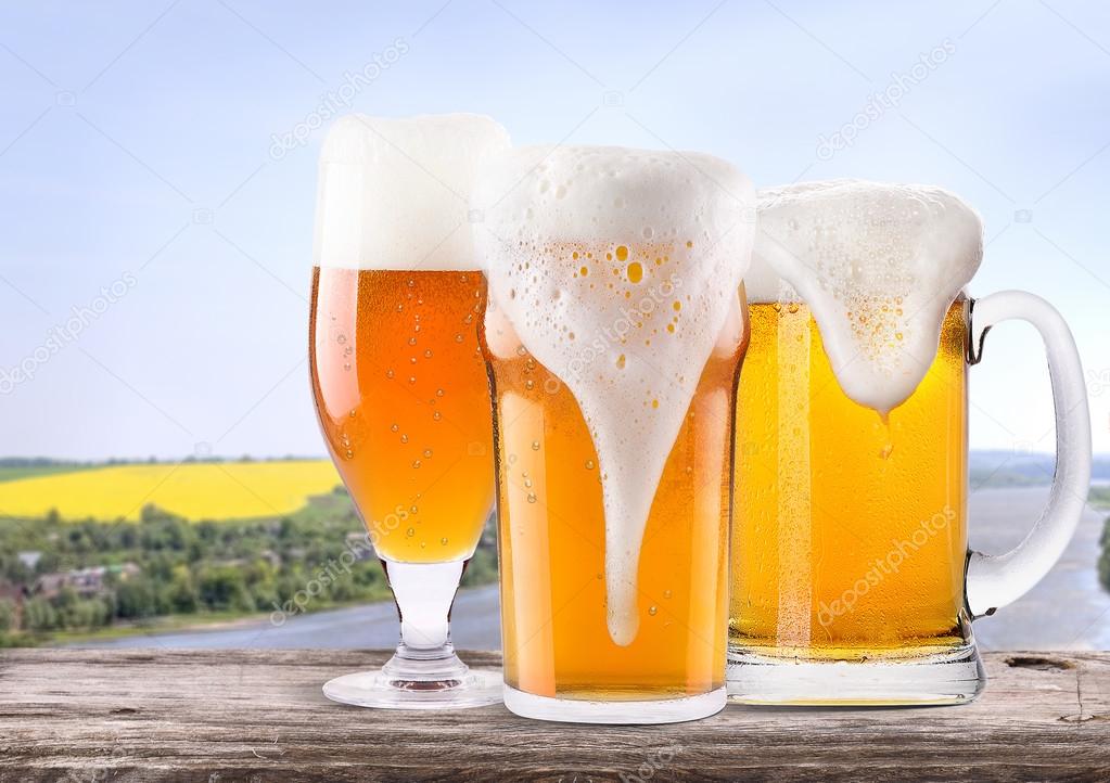 Frosty glass of light beer with summer scene background