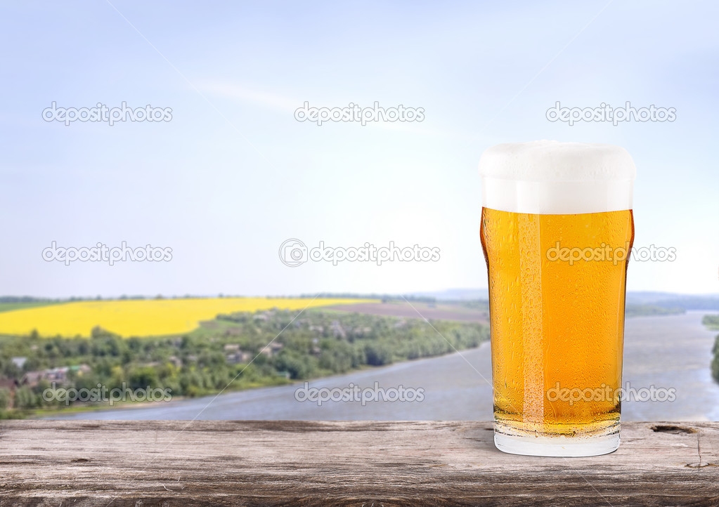 Frosty glass of light beer with summer scene background