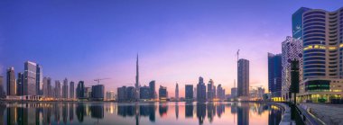 Dubai 'nin şehir manzarası ve panoramik Business Bay manzarası ve sabahları gökdelenlerin su üzerindeki yansıması, BAE.
