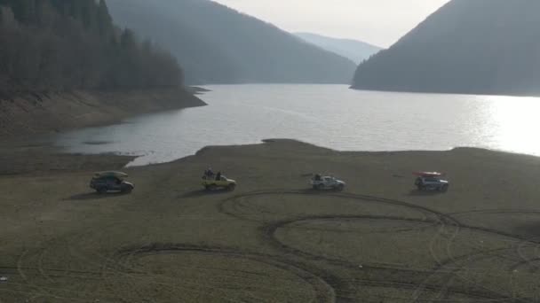 4 автомобілі їздять бездоріжжям поблизу гір та лісів. Джипи малюють візерунки на траві з колесами — стокове відео
